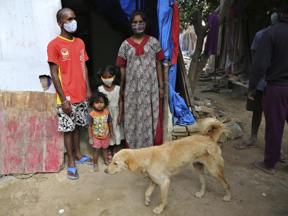 Gangaiah, left, son of Padmavathi who died of COVID-19, stands at the entrance of their family hut with his wife and children in a slum in Bengaluru, India, Thursday, May 20, 2021. Padmavathi collected hair, taking it from women's combs and hairbrushes to later be used for wigs. She earned about $50 a month. (AP Photo/Aijaz Rahi)
