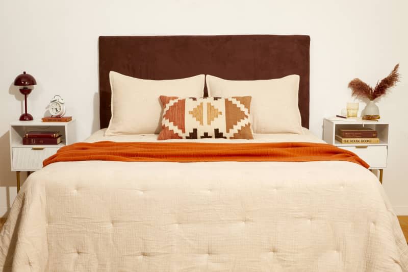 Head on shot of a bedroom with a made bed with beige bedding and the brown DIY headboard hanging behind the bed.