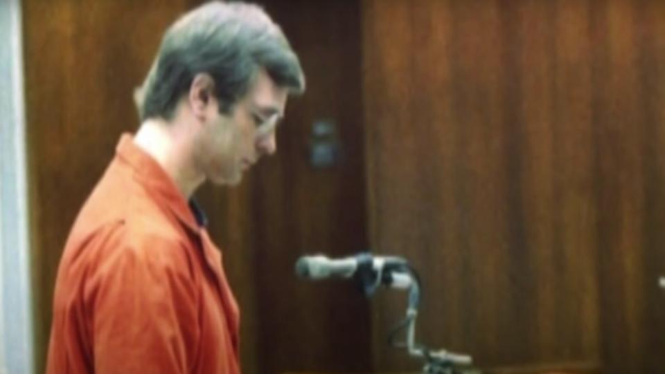 Jeffrey Dahmer stands at a microphone in a court room.