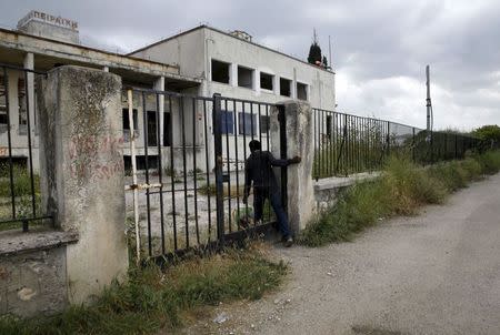A Sudanese immigrant walks climbs through a gate at a deserted textile factory in the western Greek town of Patras April 28, 2015. REUTERS/Yannis Behrakis