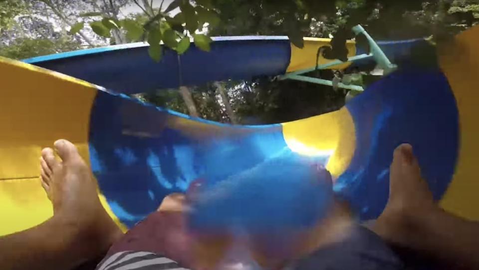 A first-person shot of two people on a mat going down a blue and yellow water slide