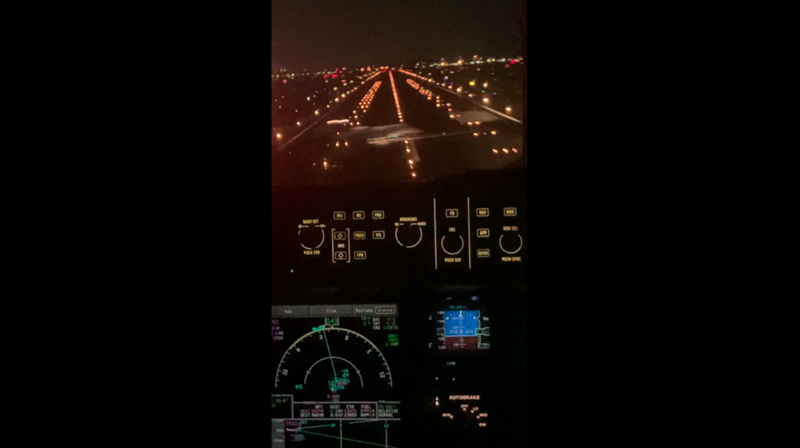 The view from a jump seat in a commercial airliner. It's night time and all you can see is a large blur directly in front of the jet with orange runway lights running off into the distance.