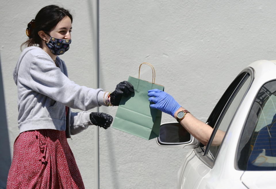 In this Thursday, April 16, 2020 photo, wearing a protective mask and gloves, budtender Alexi Ezdrin attends to a customer with curbside service at The Higher Path cannabis dispensary in the Sherman Oaks section of Los Angeles. Monday is April 20, or 4/20. That's the code for marijuana’s high holiday, which is usually marked with outdoor festivals and communal smoking sessions. But this year, stay-at-home orders have moved the party online as the marijuana market braces for an economic blow from the coronavirus crisis. (AP Photo/Richard Vogel)