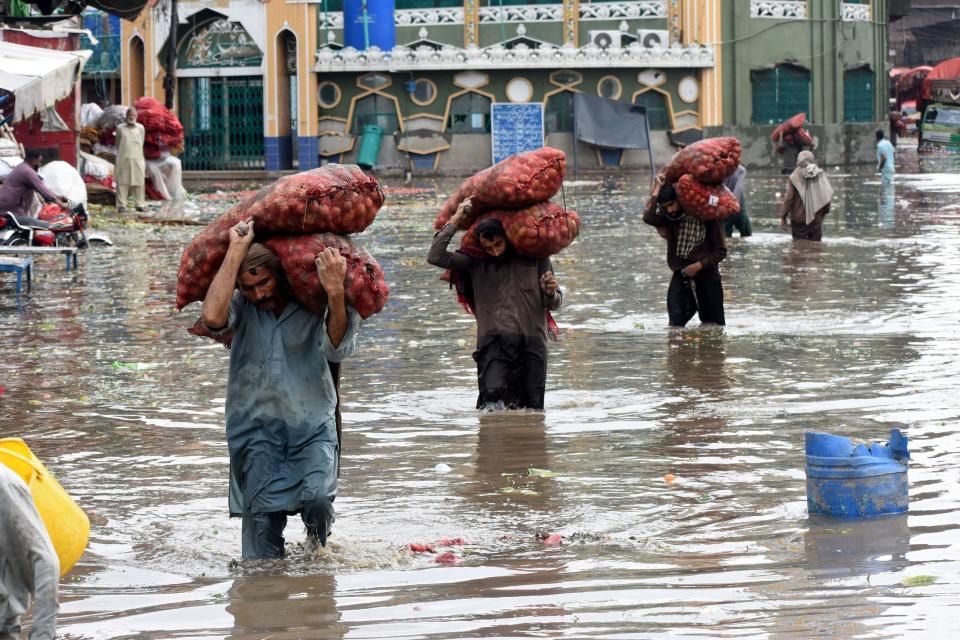 Laborers carry vegetable sacks as they wade through floodwater after heavy monsoon rains in Lahore, Pakistan, July 5, 2023. / Credit: Sajjad/Xinhua/Getty