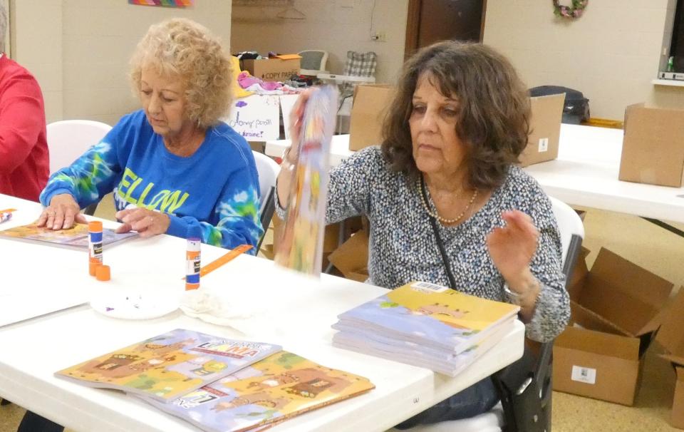 Marylin Strang, left, and Debra Orians paste children's artwork inside the covers of coloring books that will be shipped to Ukrainian children at a refugee camp in Poland.