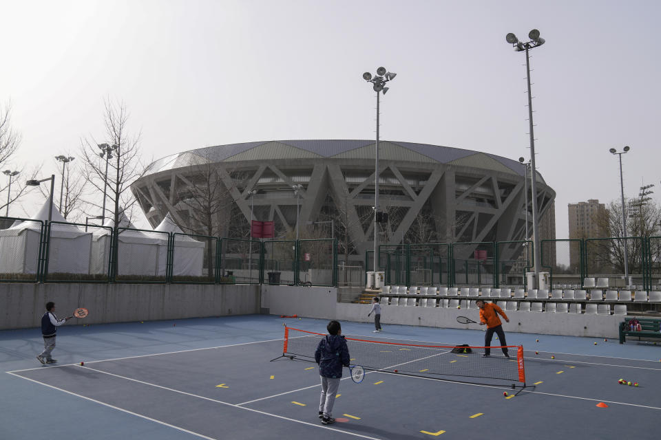 Children play tennis near the Diamond Court, background, in Beijing, Sunday, Nov. 21, 2021. Missing tennis star Peng Shuai reappeared in public Sunday at a youth tournament in the court compound, in Beijing, according to photos released by the organizer, as the ruling Communist Party tried to quell fears abroad while suppressing information in China about Peng after she accused a senior leader of sexual assault. (AP Photo/Andy Wong)