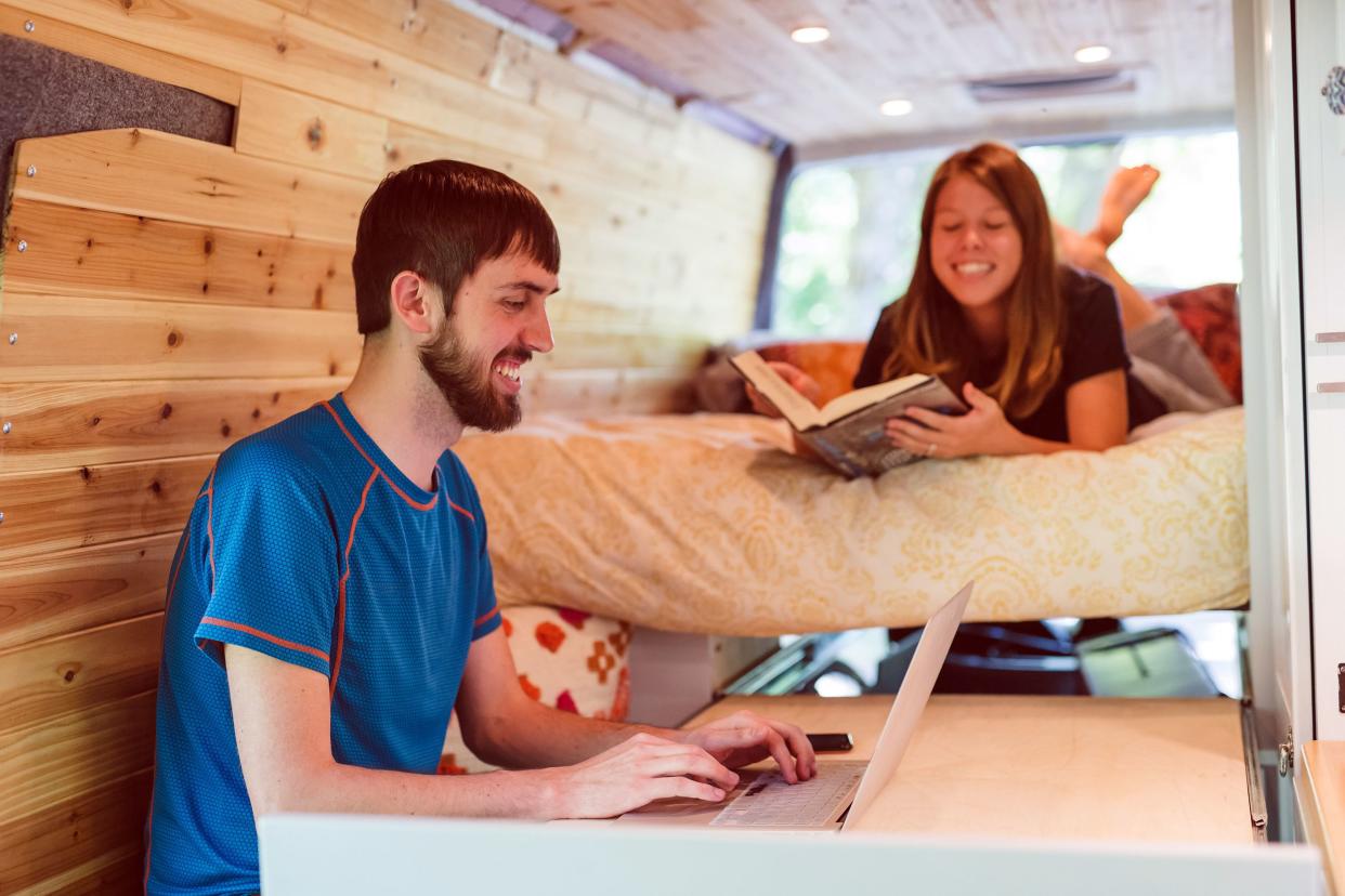 couple living in a van, man on laptop and woman is laying on bed reading book