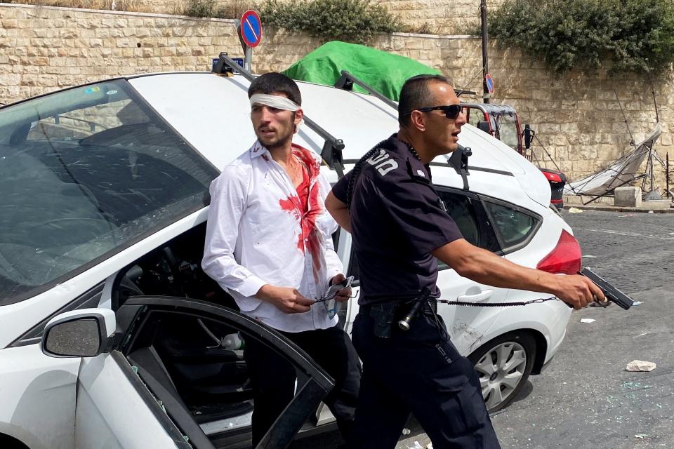 An Israeli policeman stands in front of an injured Israeli driver, moments after witnesses said a car crashed into a Palestinian on a pavementReuters