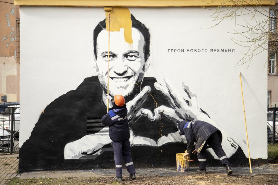 FILE - Municipal workers paint over Russia's imprisoned opposition leader Alexei Navalny in St. Petersburg, Russia, April 28, 2021. The worlds on the wall reading "Hero of our time". (AP Photo, File)