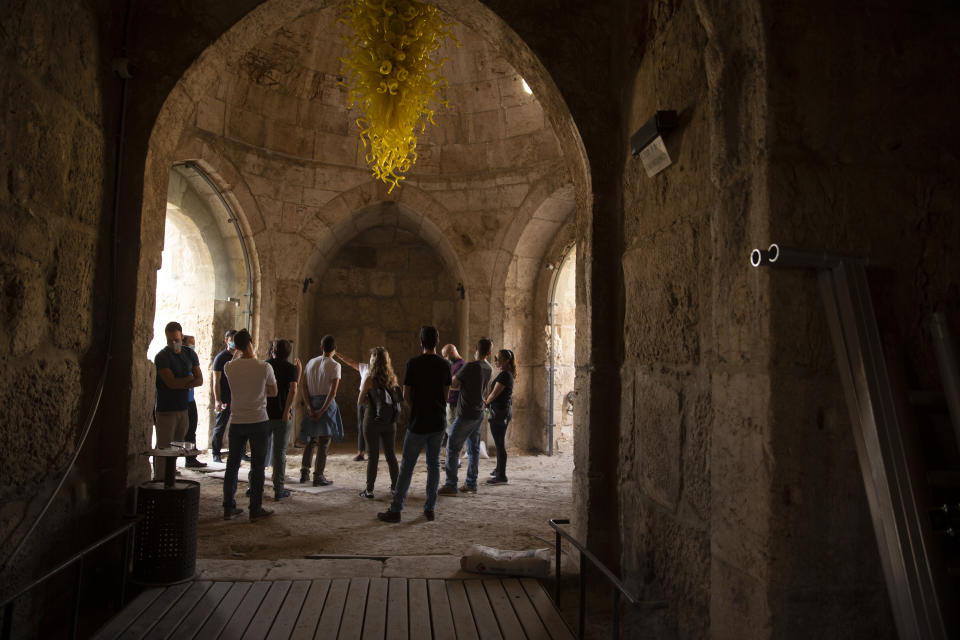 A group gathers under a work by American sculptor Dale Chihuly at the Tower of David Museum in the Old City of Jerusalem, Wednesday, Oct. 28, 2020. The ancient citadel is devoid of tourists due to the pandemic and undergoing a massive restoration and conservation project. (AP Photo/Maya Alleruzzo)