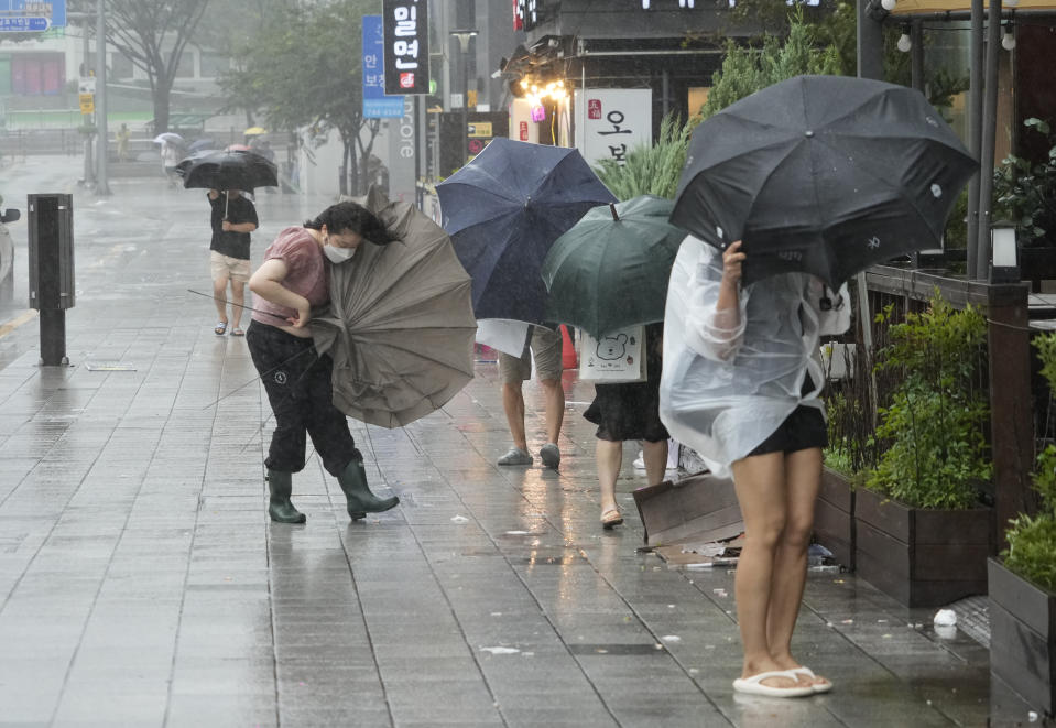 People struggle to hold onto their umbrellas in the rain and wind as the tropical storm named Khanun approaches to the Korean Peninsular, in Busan, Thursday, Aug. 10, 2023. (AP Photo/Ahn Young-joon)