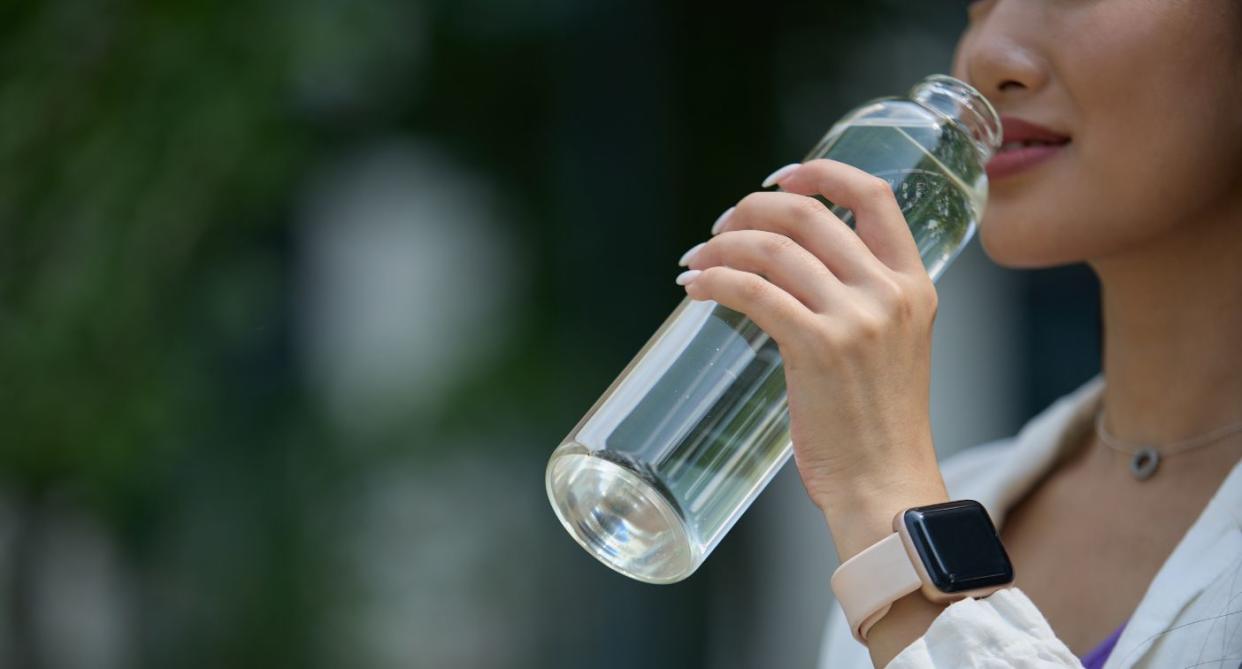 Woman drinking from glass water bottle to reduce toxin exposure. (Getty Images)