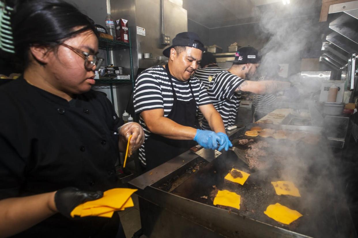 Kitchen staff smashes beef patties and assembles burgers.