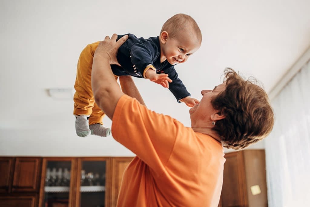 A nanny lifts a smiling baby up in the air.