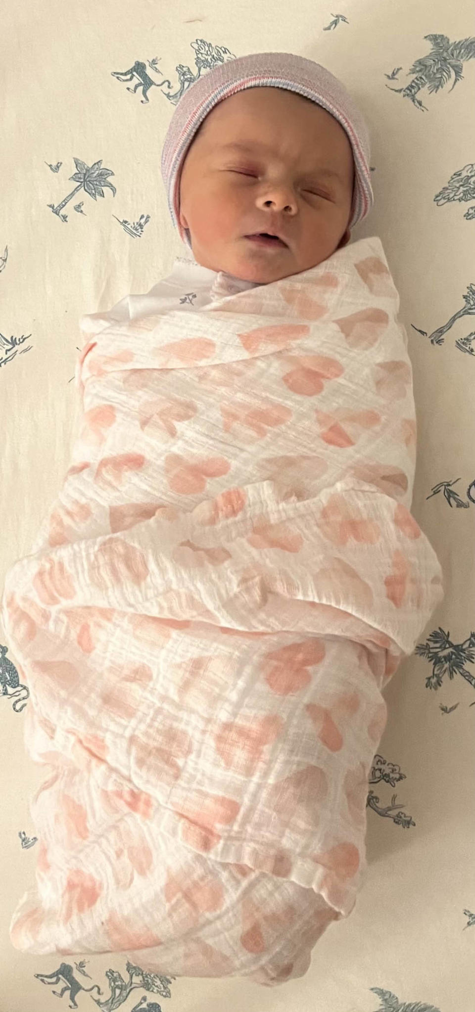 A baby on white and blue sheets swaddled in a white blanket with pink hearts. (Courtesy of Nicole Wallace)