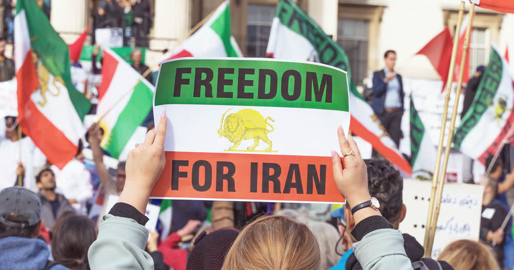 This post is about the LGBTQ+ community in Iran. In the photo, a person holding a banner with the Iranian flag and a message that reads 