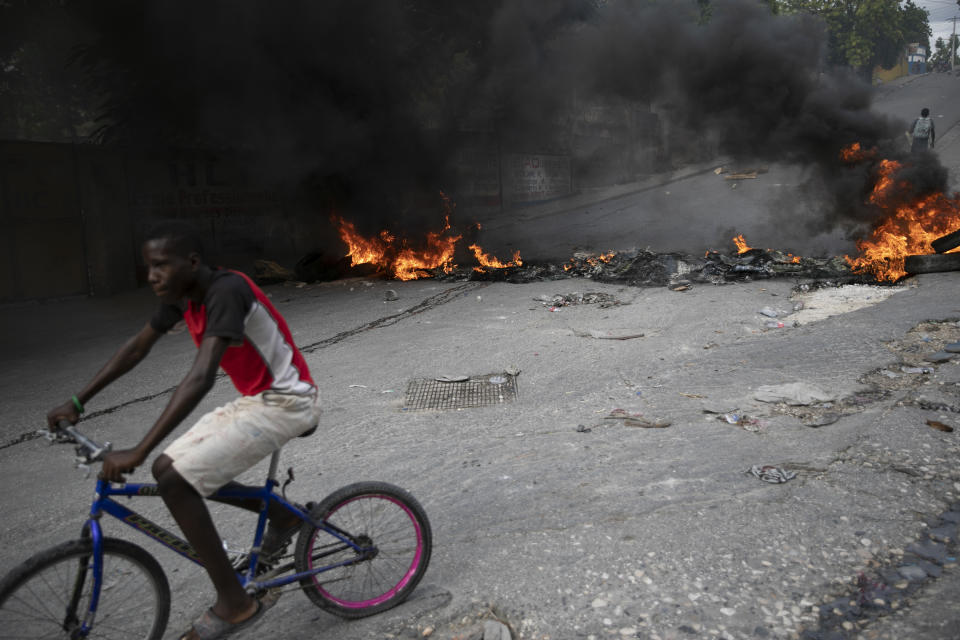 A man rides his bicycle a burning barricade during a protest over the death of journalist Romelo Vilsaint, in Port-au-Prince, Haiti, Sunday, Oct. 30, 2022. Vilsaint died Sunday after being shot in the head when police opened fire on reporters demanding the release of one of their colleagues who was detained while covering a protest, witnesses told The Associated Press. (AP Photo/Odelyn Joseph)