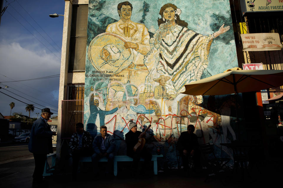 Men sit outside a store in front of the mural “El Corrido de Ricardo Valdez,” painted in 1994 by Juan Solis, in Mariachi Plaza in February in Boyle Heights, Los Angeles. (Photo: Patrick T. Fallon for Yahoo News)