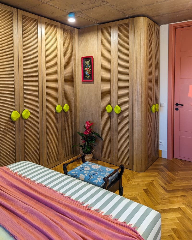 Bedroom with tree branch wallpaper wall, parquet wood floor, wall of wood closets, and pops of yellow and orange