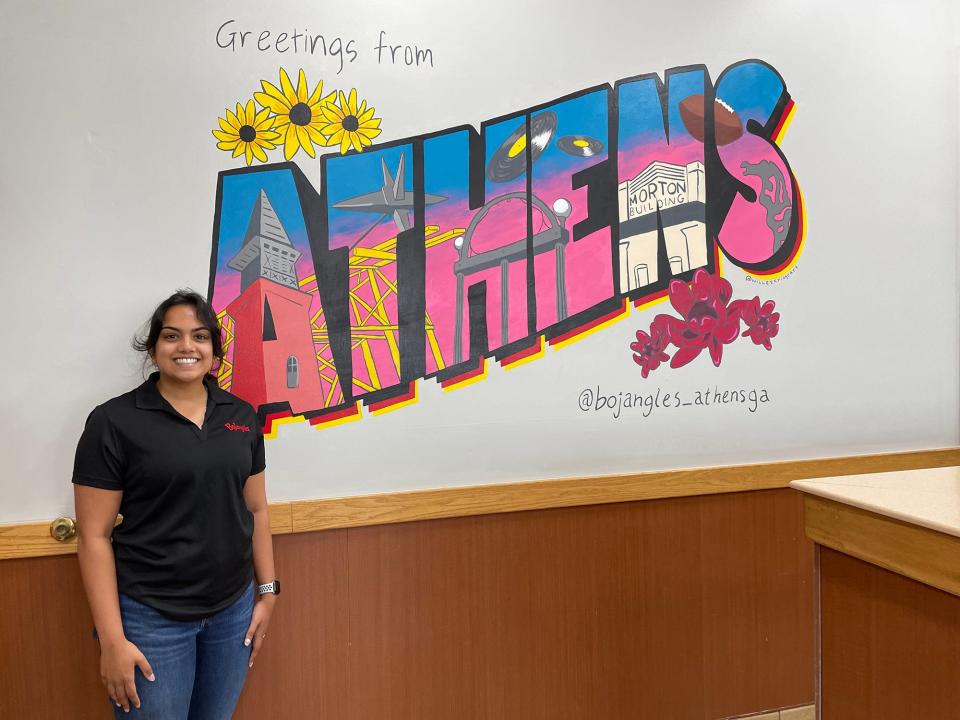 Lela Dinakaran, director of marketing for the Atlanta Highway Bojangles location, stands in front of Will Eskridge's postcard mural inside the restaurant on Jun. 30, 2022.