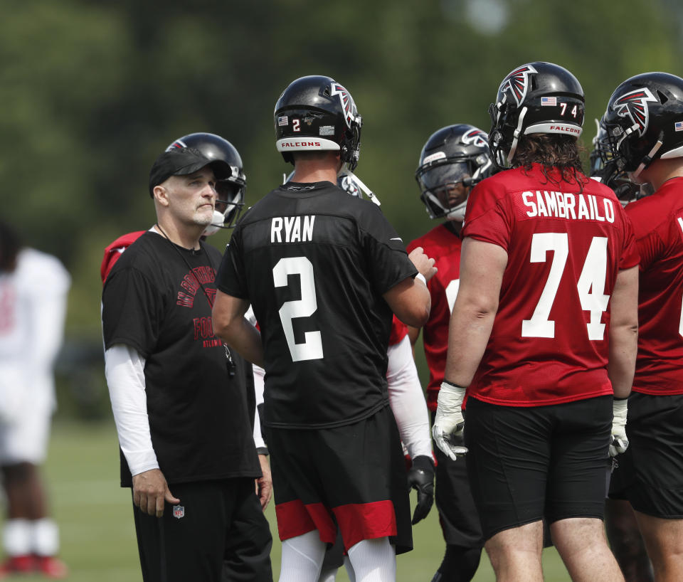 Atlanta Falcons head coach Dan Quinn looks on as quarterback Matt Ryan talks in the huddle during their NFL training camp football practice Monday, July 22, 2019, in Flowery Branch, Ga.(AP Photo/John Bazemore)