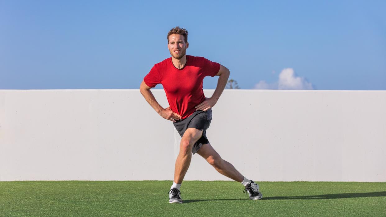  Man outdoors on grass performing a single leg squat variation with hands on hips and right leg extended behind left. 