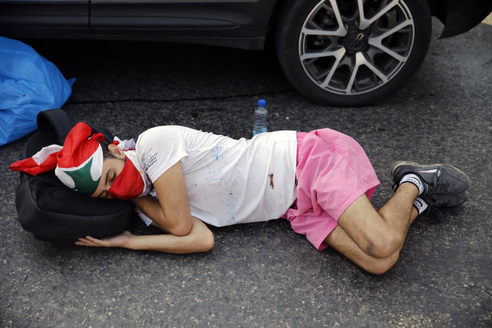 An anti-government protester sleeps on the ground as others block a road leading to the Presidential Palace in Baabda, east of Beirut, Lebanon, Wednesday, Nov. 13, 2019. Lebanese protesters said they will remain in the streets despite the president's appeal for them to go home. (AP Photo/Bilal Hussein)