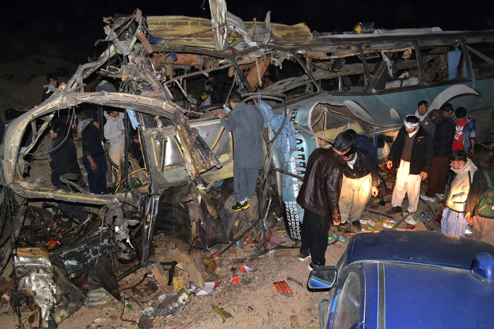 People look at the wreckage of a passenger bus destroyed in a bomb blast in the Mastong district, near Quetta, Pakistan, Tuesday, Jan. 21, 2014. A roadside car bomb hit a bus of Shiite pilgrims returning from Iran, killing several people and wounding many, in restive Baluchistan province, said a top security official. (AP Photo/Arshad Butt)