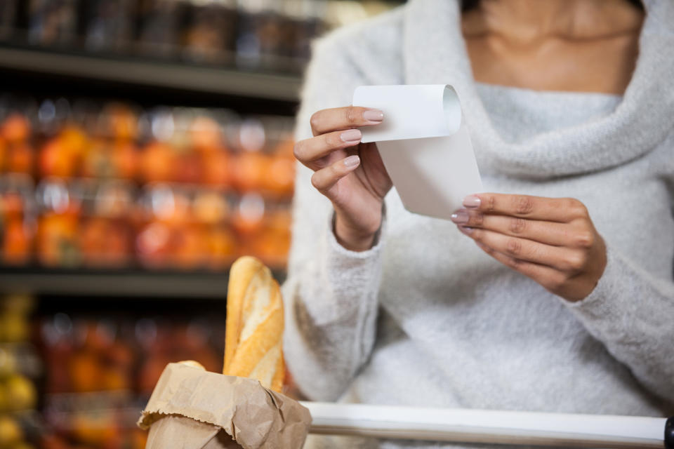 Mid section of woman holding bill in grocery section of supermarket