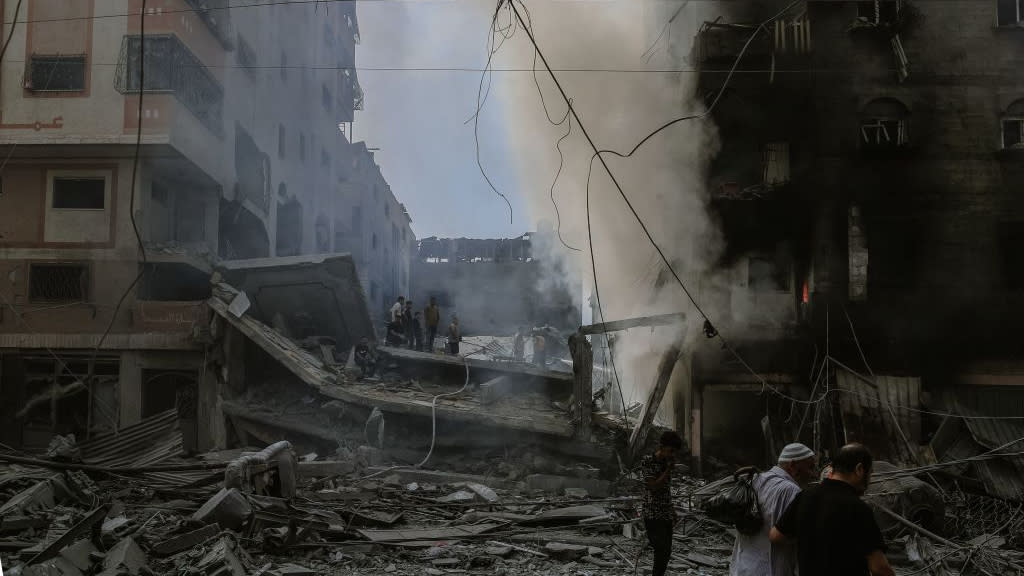  Gazans walk by ruins of buildings from Israeli airstrikes. 