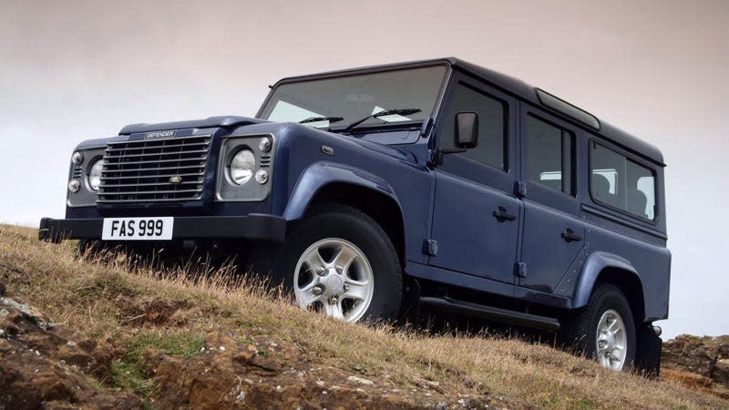 A photo of a dark blue Land Rover Defender driving on grass. 