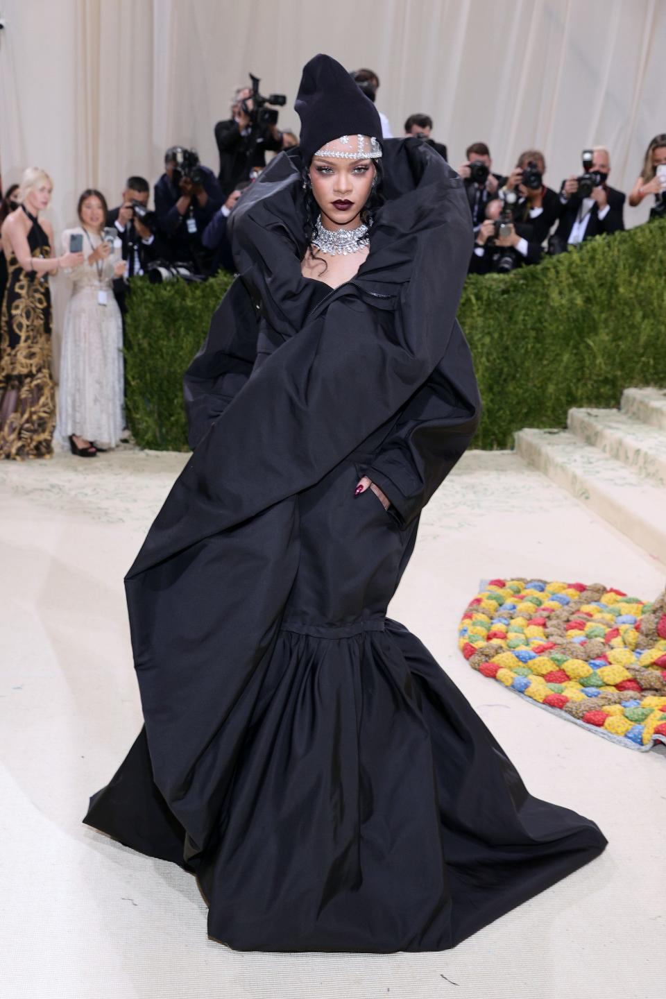 Rihanna at the 2021 Met Gala wearing an oversized black coatdress and diamond necklace.