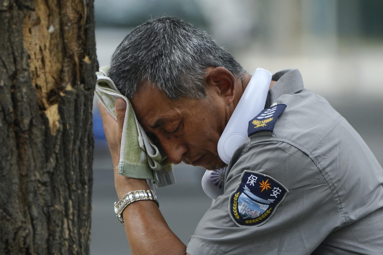 A security guard wears an electric fan around his neck and wipes his sweat.