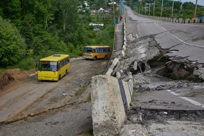 Buses carrying refugees drive past a damaged bridge near Kharkiv (EPA)