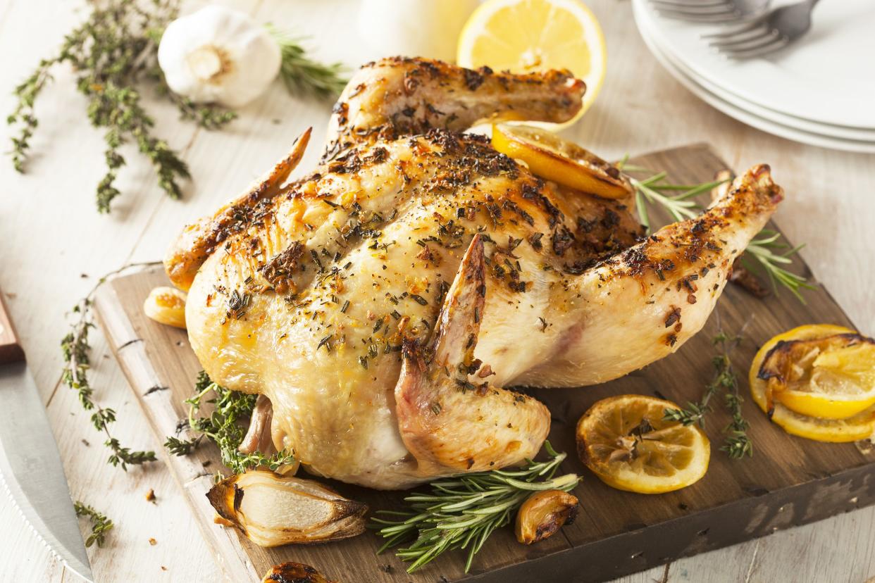 Herb-and-lemon-roasted chicken on a cutting board with a serving knife and forks and plates on a wooden table