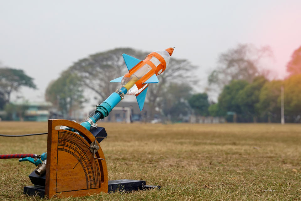 Plastic bottle water rocket, mounted on a wooden launcher, ready for takeoff in an open field with trees in the background