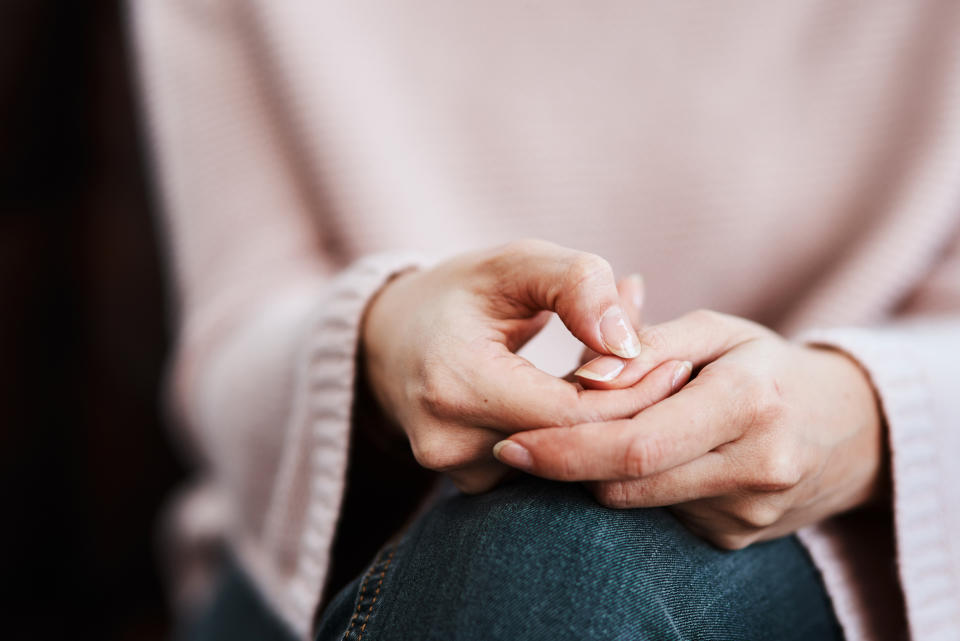 Close-up of a person sitting with hands nervously fidgeting a small object, indicating stress or deep thought