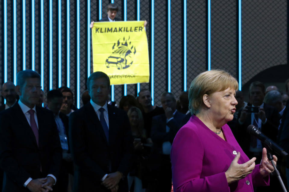 German Chancellor Angela Merkel speaks as a Greenpeace activist standing ontop of a displayed car protests against the global warming at the international Frankfurt Motor Show (IAA) in Frankfurt, Germany, September 12, 2019. REUTERS/Ralph Orlowski