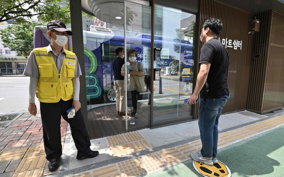 A man checks his temperature in front of a thermal imaging camera before being allowed to enter one of the newly installed bus stops - JUNG YEON-JE /AFP