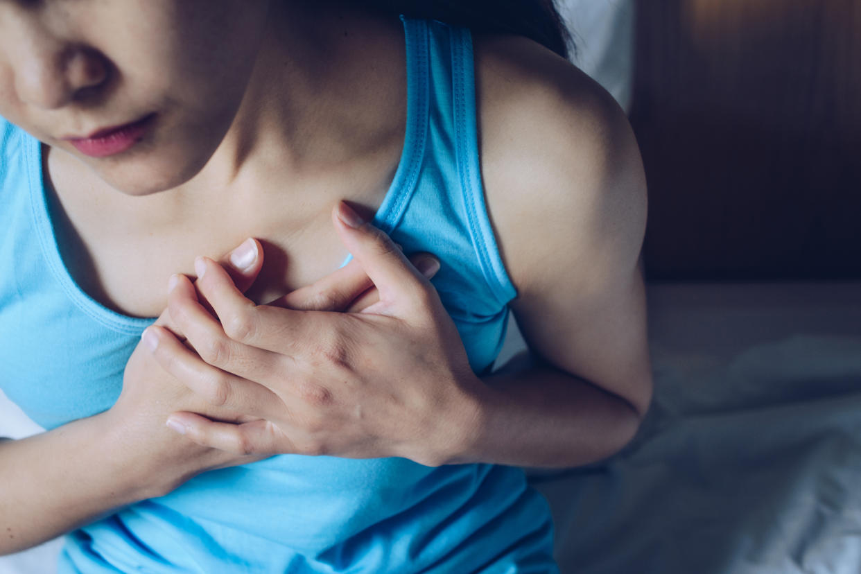 A young woman holds both hands over her heart.