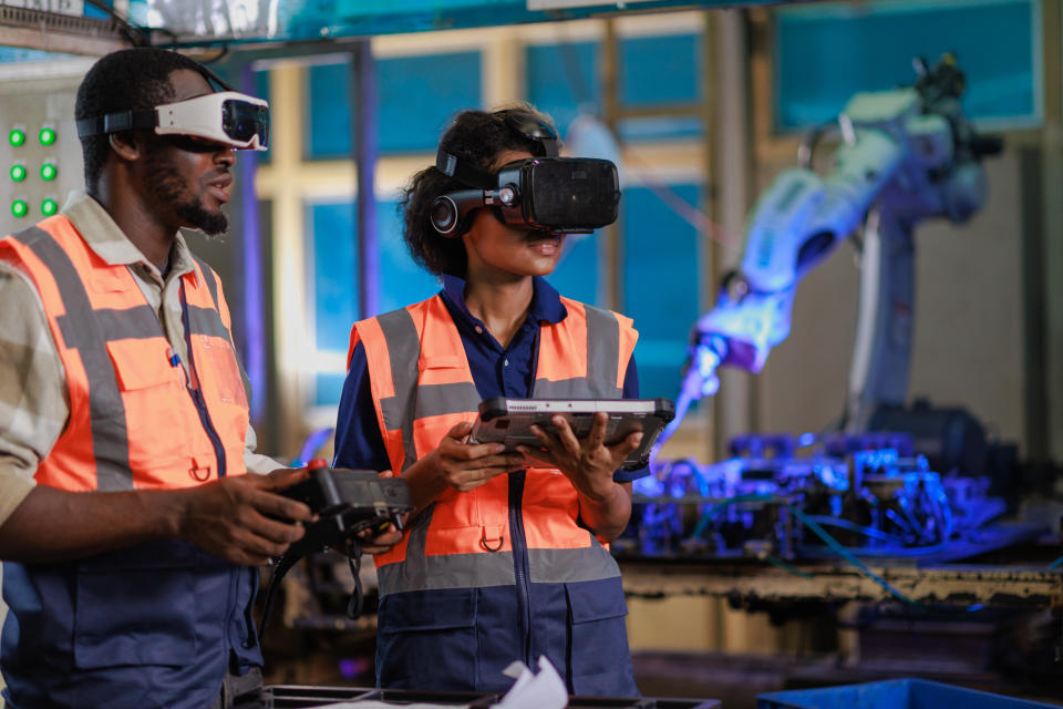 AI Two African engineer using vr Glasses for controlling the robotic welding  arm in the factory production line.