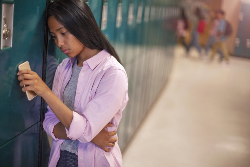 Lonely teenage girl leaning on metallic locker