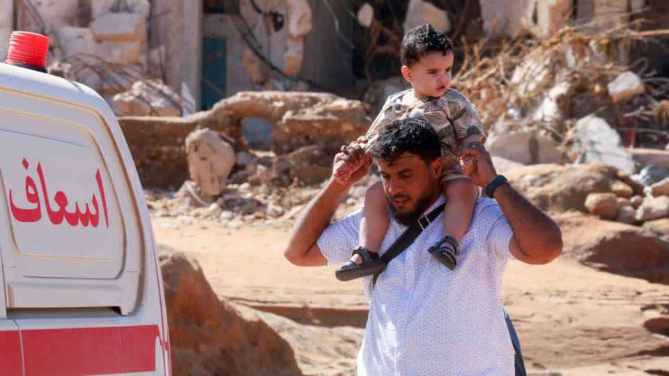 A man carries a child on his shoulder as he walks past a flash flood-damaged area in Derna on September 14, 2023. - Abdullah Doma/AFP/Getty Images