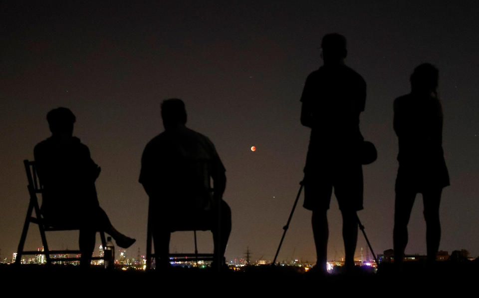 People in a field watch&nbsp;the moon over the skyline of Frankfurt, Germany. (Photo: Kai Pfaffenbach / Reuters)