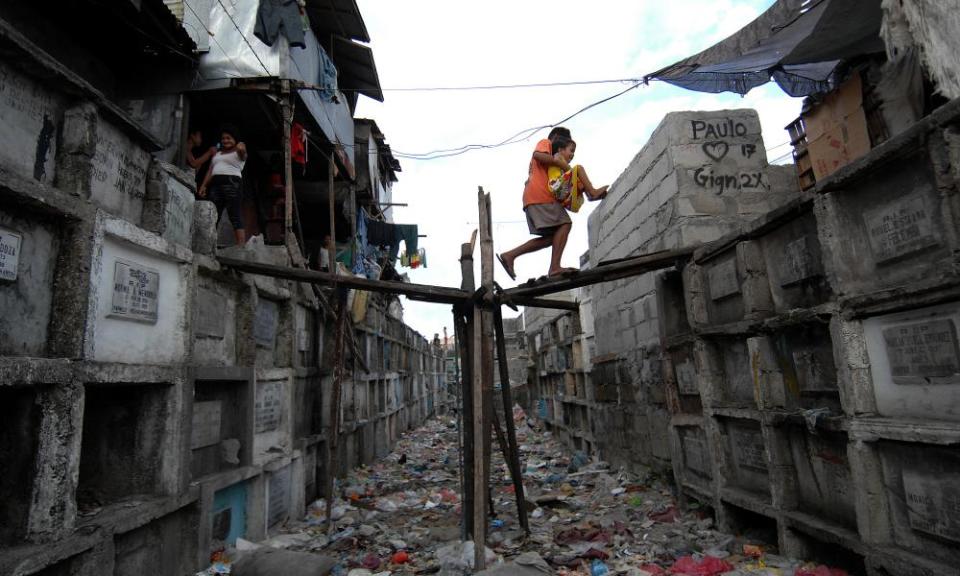 Filipino children cross a bridge over a rubbish filled corridor passing from one block of tombs to another inside the Municipal Cemetery of Navotas, north of Manila, where they live.