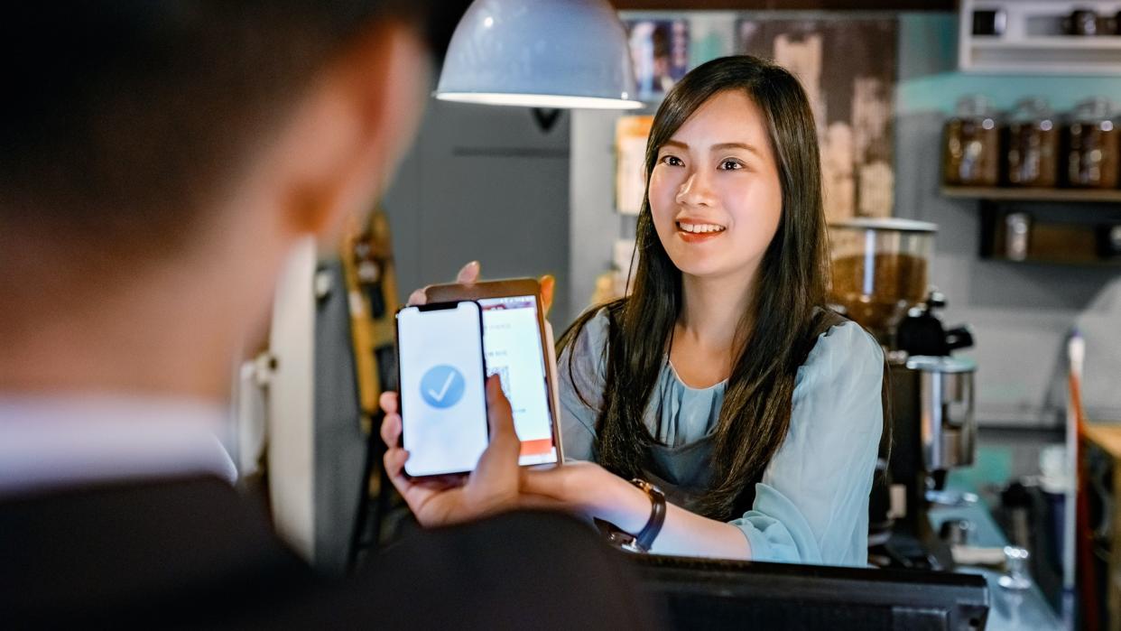 Smiling female cashier holding digital tablet at checkout.