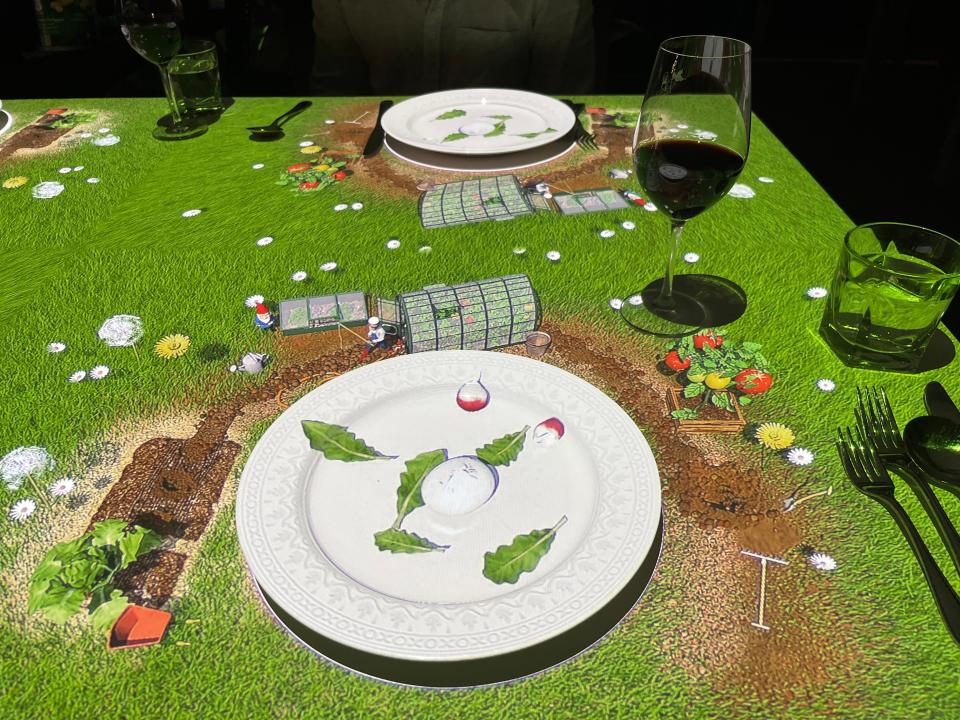 The table with white plates at Le Petit Chef, light up green with an outdoor sketch