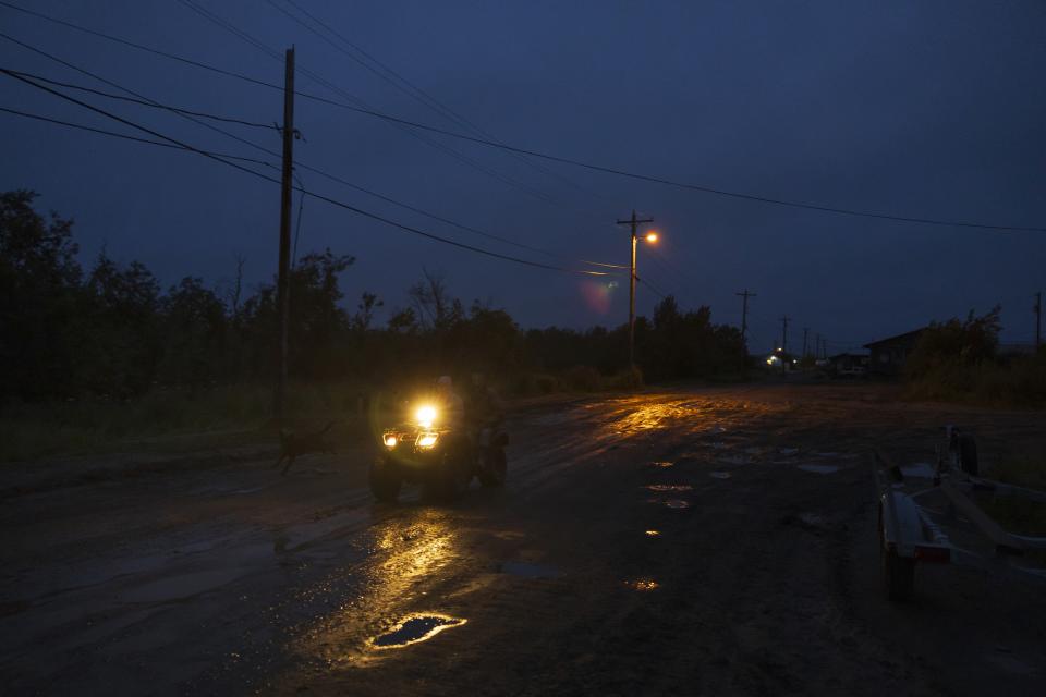 A villager rides an ATV vehicle along Main Street following evening rainfall, Sunday, Aug. 20, 2023, in Akiachak, Alaska. Most of the village's nearly 700 people are getting modern plumbing for the first time this spring and summer — and finding their lives transformed. (AP Photo/Tom Brenner)