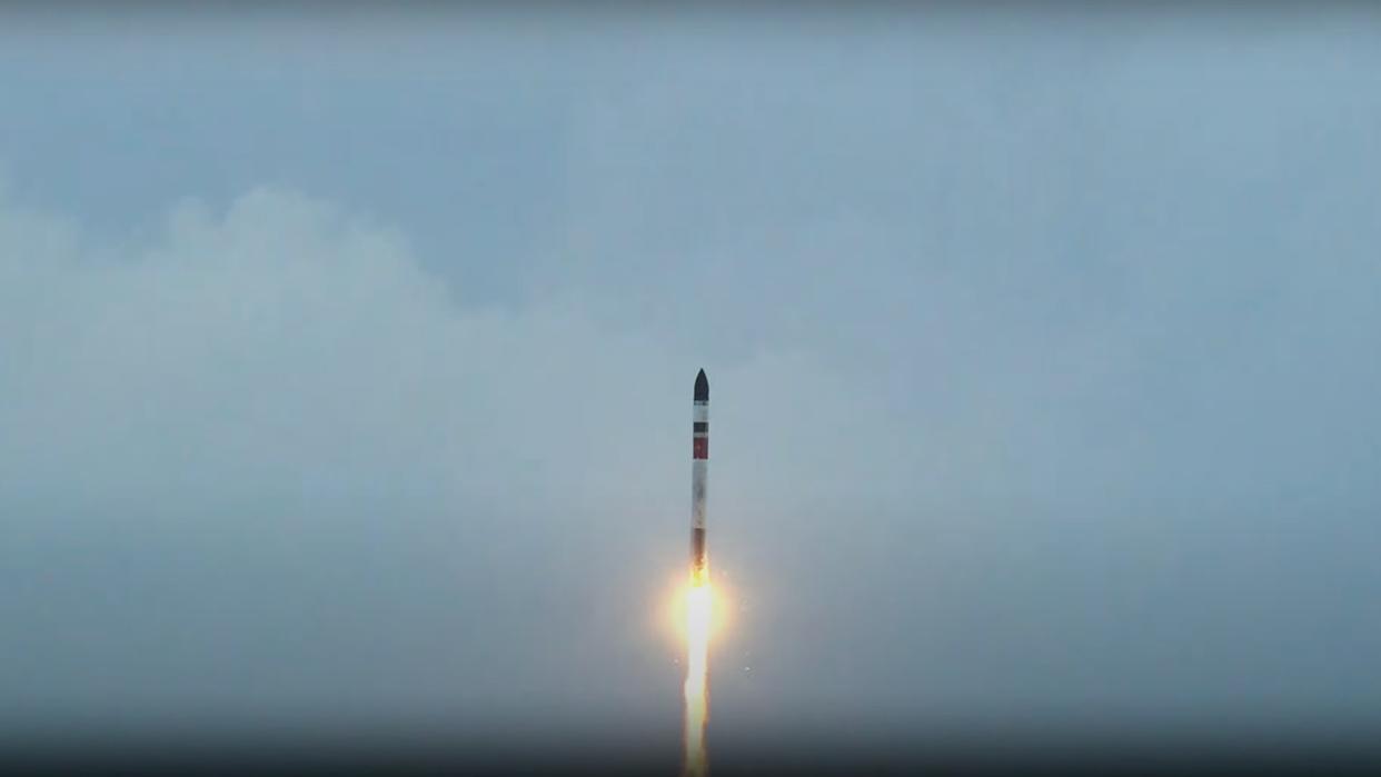  A white, red and green rocket launches into a cloudy sky. 