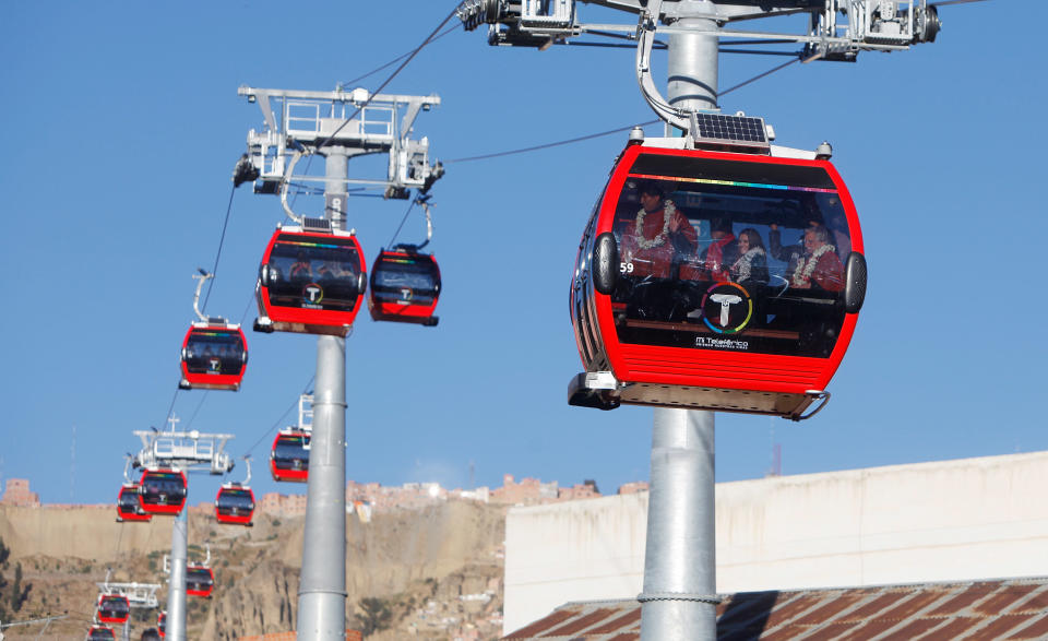 Bolivia's President Evo Morales waves to supporters from inside the cable car on the right, during the inauguration ceremony of the world's highest cable car service that links the city center with its neighbor El Alto, in La Paz, Bolivia, Friday, May 30, 2014. Morales, whose government funded the work, opened the service in a festive atmosphere, making an offering to the Pachamama or Mother Earth, and boarded the lead cable car with Vice President Alvaro Garcia, seated on the right. (AP Photo/Juan Karita)